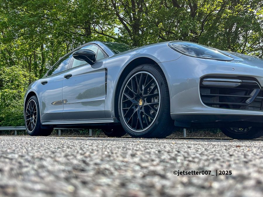 A silver Porsche photographed from very low on tarmac, with green trees behind